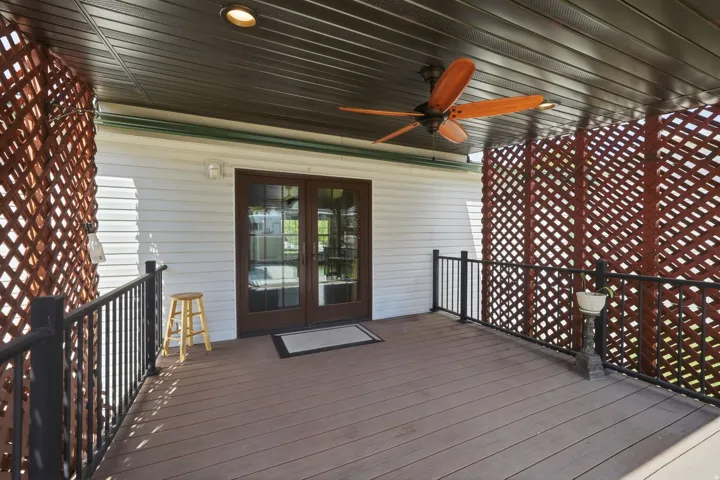 Covered porch featuring wood-finish decking and a dark slatted ceiling with an integrated ceiling fan