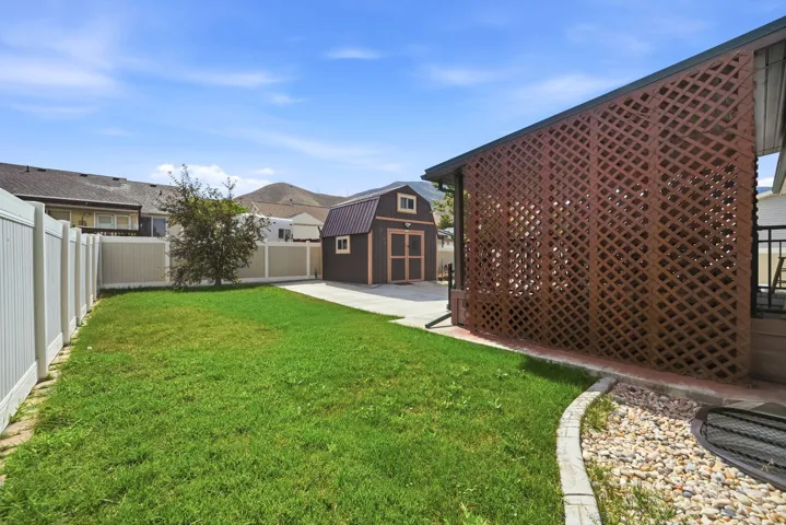 Manicured lawn with a detached storage shed, full privacy fencing, and a lattice-screened patio