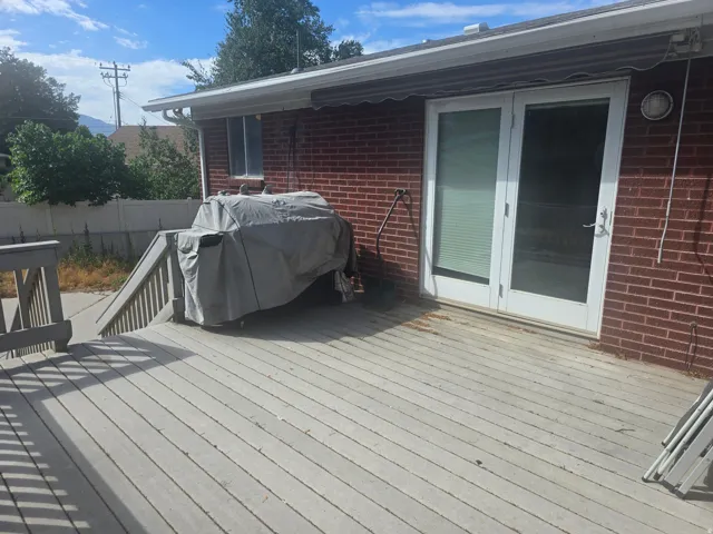 Spacious outdoor deck with a red brick exterior, featuring white double glass doors, a window, and a white gutter system
