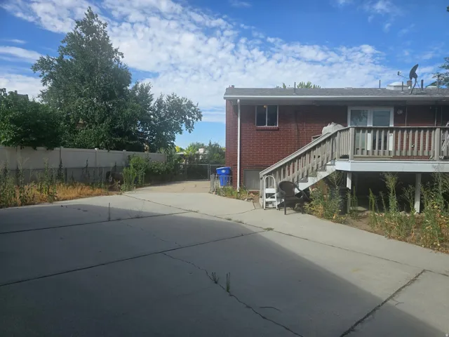 Rear exterior with red brick facade, an upper-level wooden deck with stairs, a concrete patio, and a privacy fence