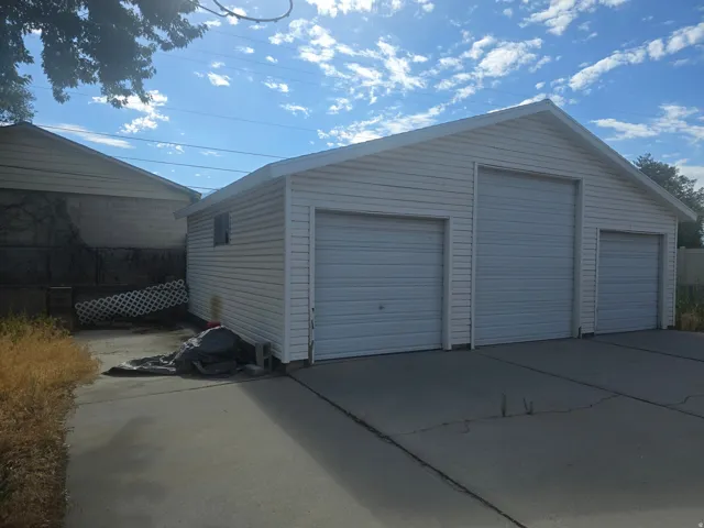 Detached three-car garage featuring white vinyl siding, a pitched roof, and concrete driveway apron
