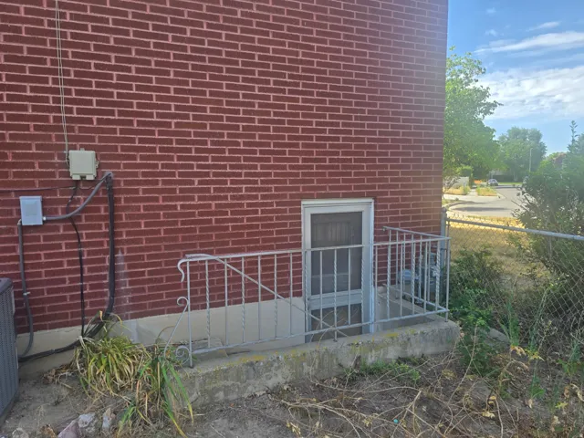 Red brick exterior featuring a white-framed basement window and metal handrails