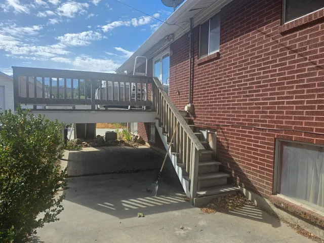 Exterior brick facade featuring an elevated wood deck with railing and stairs