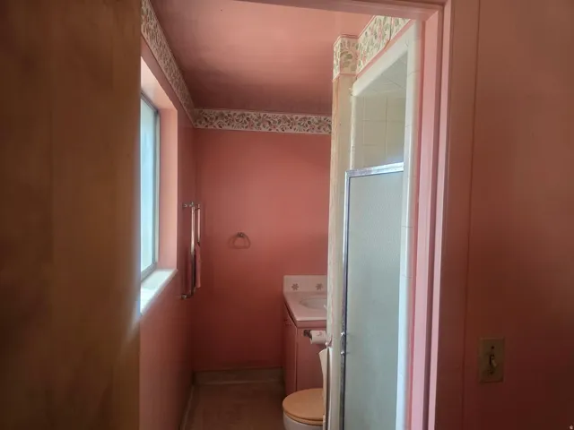 Full bathroom featuring a window, vanity with integrated sink, toilet, and a stand-up shower with a glass enclosure