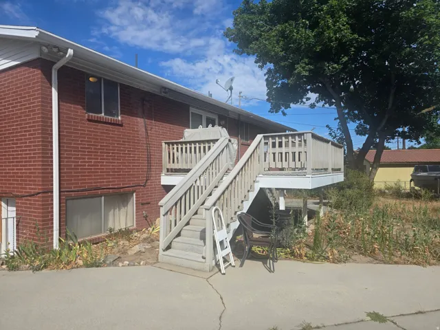 Red brick exterior featuring a multi-level wood deck with stairs, a concrete patio, and mature trees