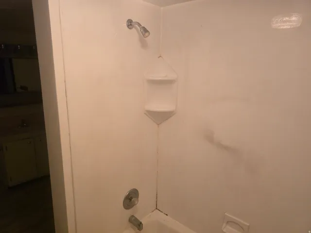 White acrylic tub and shower combination with an integrated corner caddy and chrome fixtures