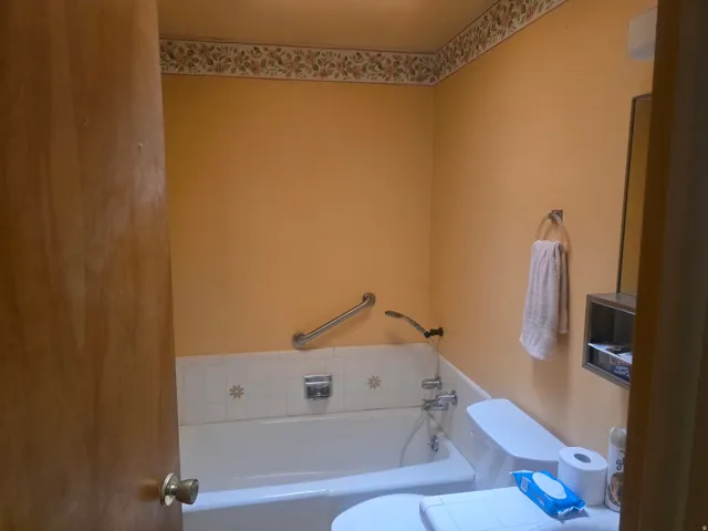 Bathroom featuring a white bathtub with tile surround, a wall-mounted grab bar, and a toilet