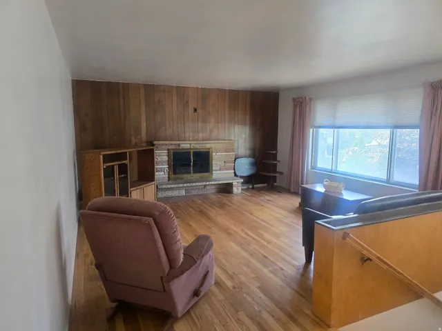 Living area featuring wood-finish flooring, a wood-paneled accent wall, and a brick-surround fireplace with a metal insert