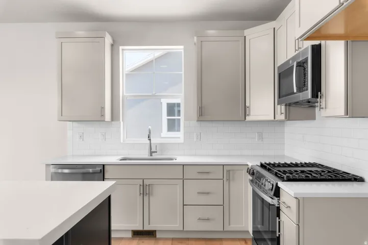 Kitchen featuring light grey cabinetry, white countertops, subway tile backsplash, stainless steel appliances, and a window above the sink