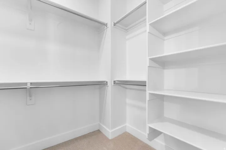 Custom closet system featuring white shelving units, multiple chrome hanging rods, and light-toned carpet flooring