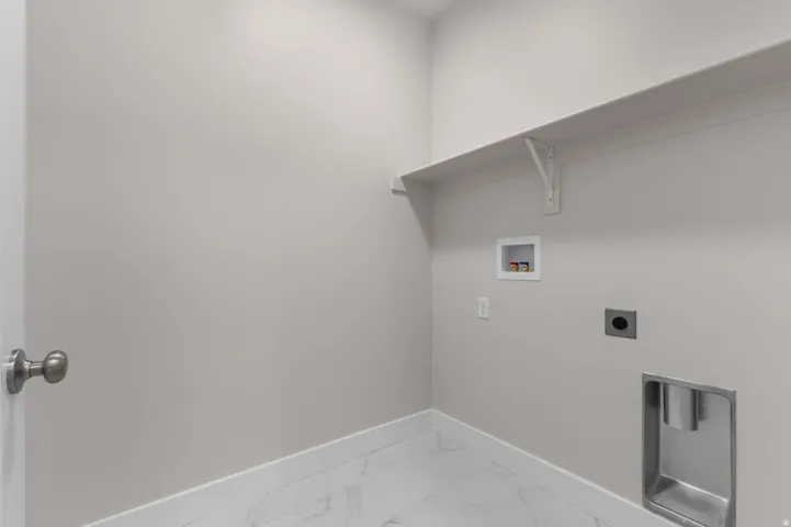 Dedicated laundry area featuring a built-in shelf, marble-look tile flooring, and neutral wall paint