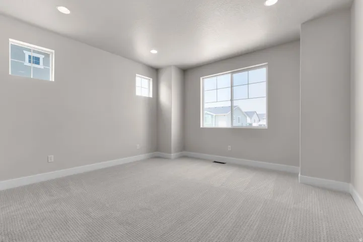 Spacious interior room featuring light gray carpet, multiple windows including a large main window and two smaller inset windows, white baseboards, and recessed ceiling lighting