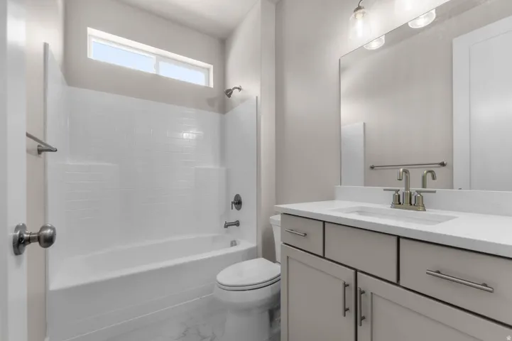Bathroom featuring a white bathtub with subway tile surround, an overhead transom window, and a gray vanity with a white countertop and undermount sink