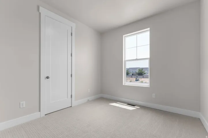 Carpeted room featuring a white interior door with contemporary trim, a large window with white framing, light neutral wall paint, and white baseboards