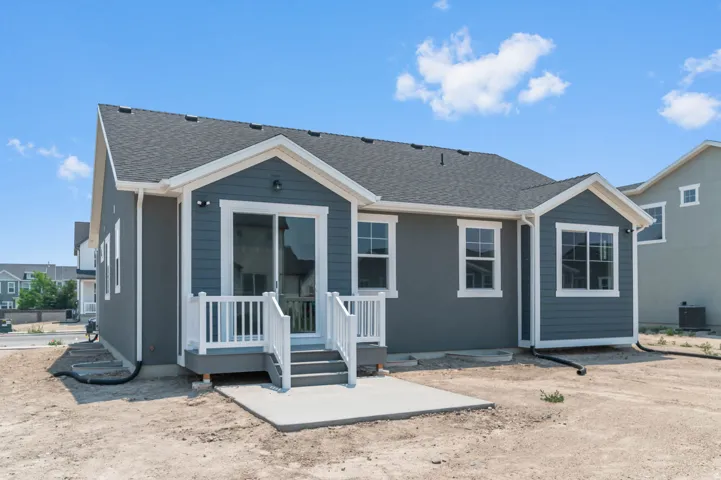 Rear exterior featuring a sliding glass door, private concrete patio, white railing, and grey siding with white trim