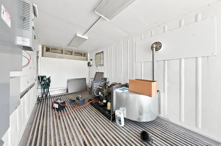 Utility space featuring corrugated metal walls and flooring, overhead fluorescent lighting, and visible mechanical equipment