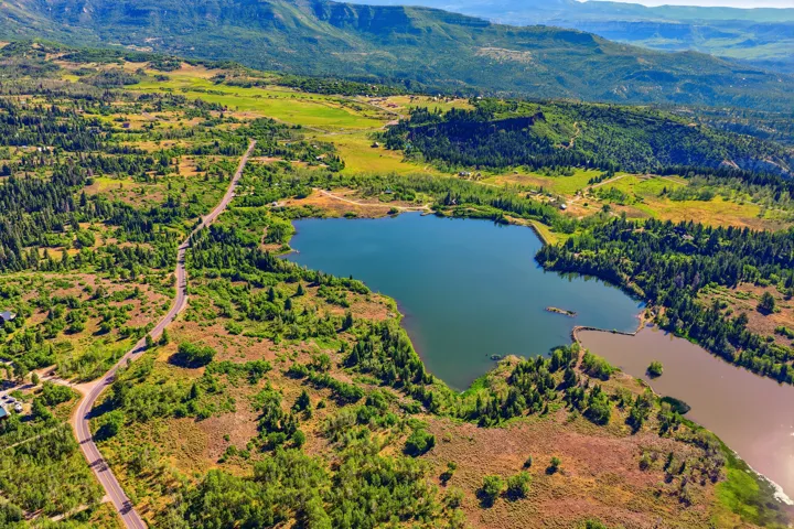 Expansive aerial landscape featuring a large body of water surrounded by lush green and autumnal foliage