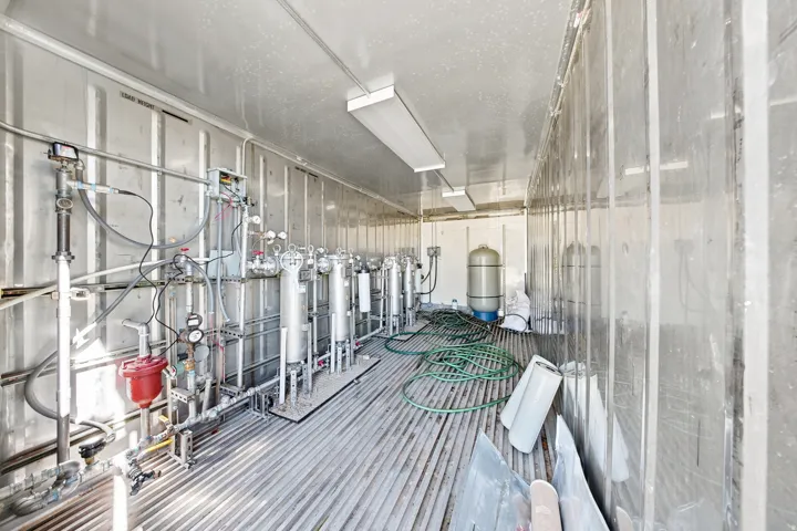 Industrial interior featuring extensive piping, gauges, and filtration equipment within a corrugated metal structure