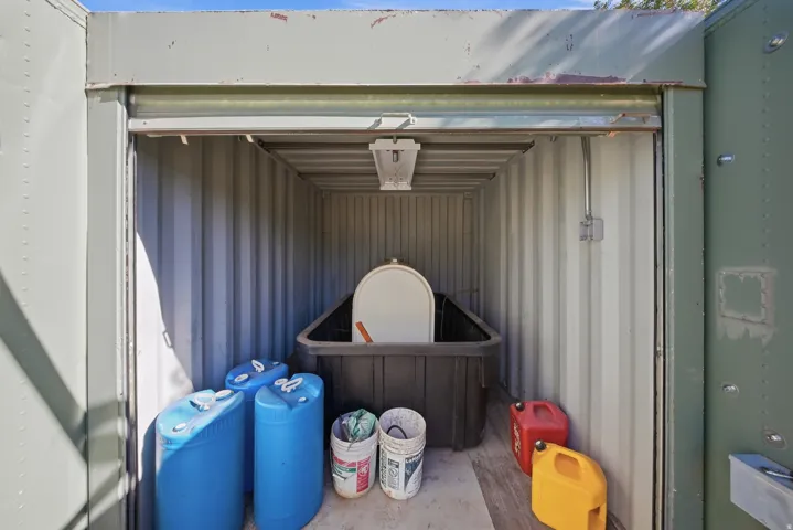 Interior of a corrugated metal storage container featuring a roll-up door, overhead lighting, and electrical conduit Diesel generator storage