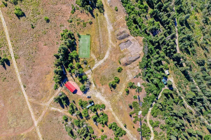 Extensive rural property featuring a red-roofed building, a tennis court, and multiple dirt paths, surrounded by both dense and sparse tree coverage
