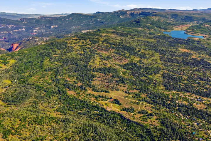 Expansive mountainous terrain featuring dense forests, scattered clearings, a distant body of water, and a red rock canyon formation