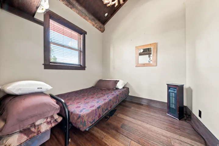 Room featuring wood-finish flooring, a window with wood trim, and a high, exposed wood beam ceiling