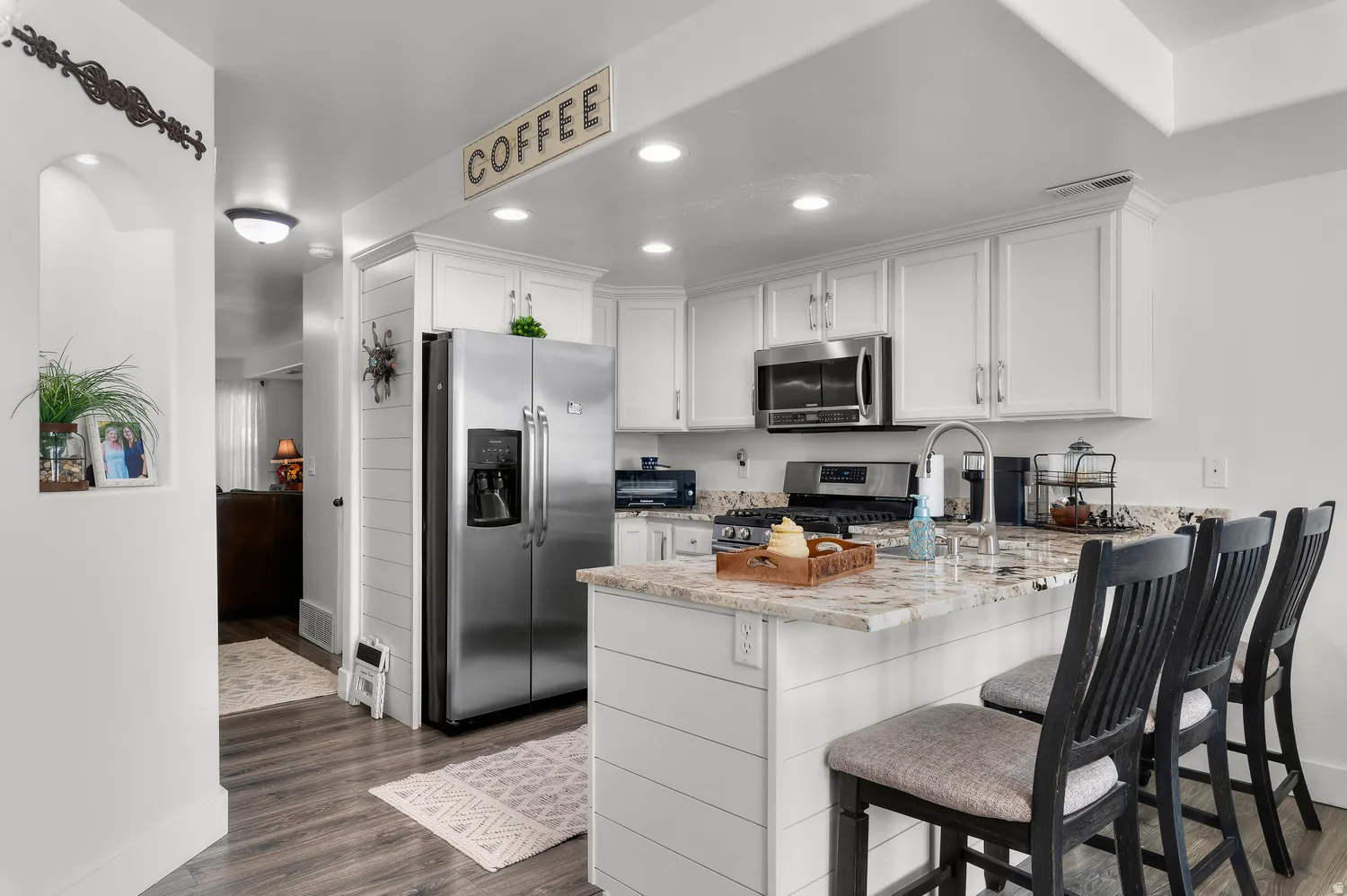 Modern kitchen featuring white cabinetry, granite countertops, stainless steel appliances, wood-finish flooring, and recessed lighting