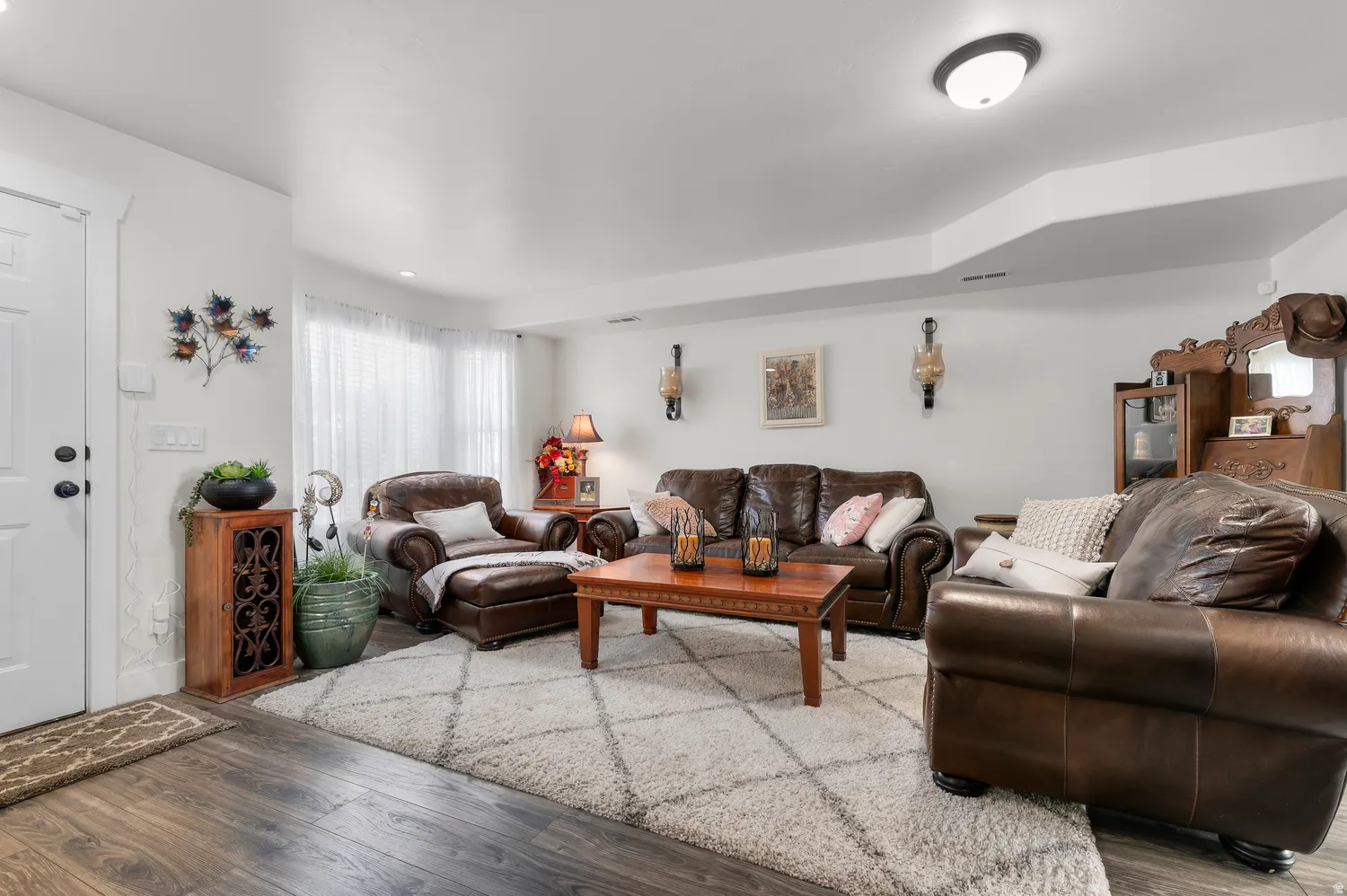 Bright living area with wood-finish flooring, a tray ceiling detail, and a prominent bay window
