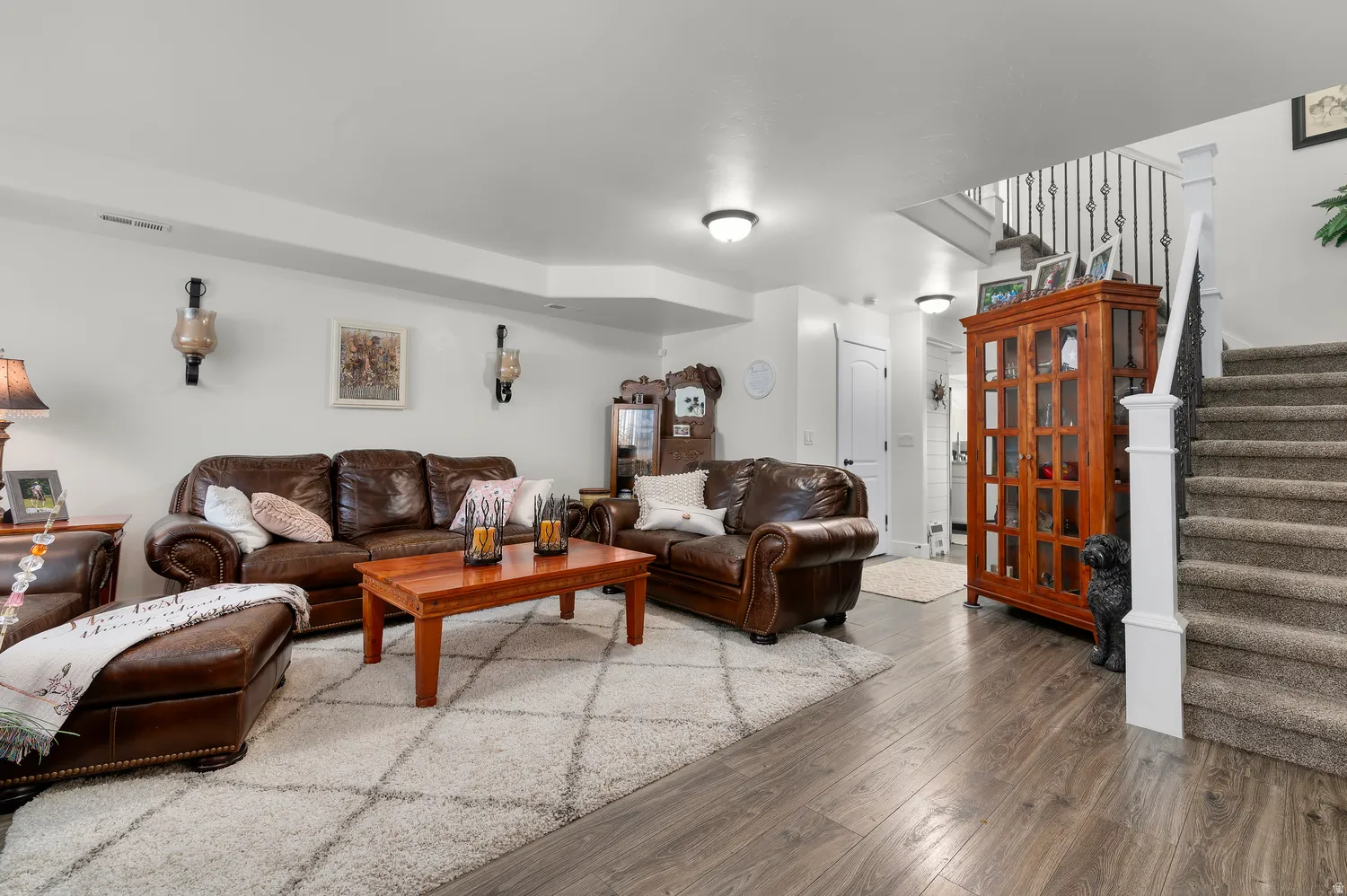 Spacious living area featuring wood-finish flooring and a carpeted staircase with wrought iron balusters