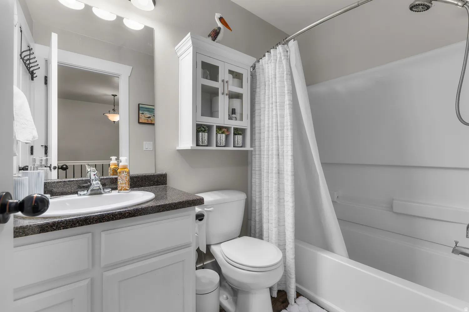Bathroom featuring a white vanity with a dark countertop and undermount sink, a toilet, a built-in white cabinet with glass doors, and a bathtub with a shower curtain