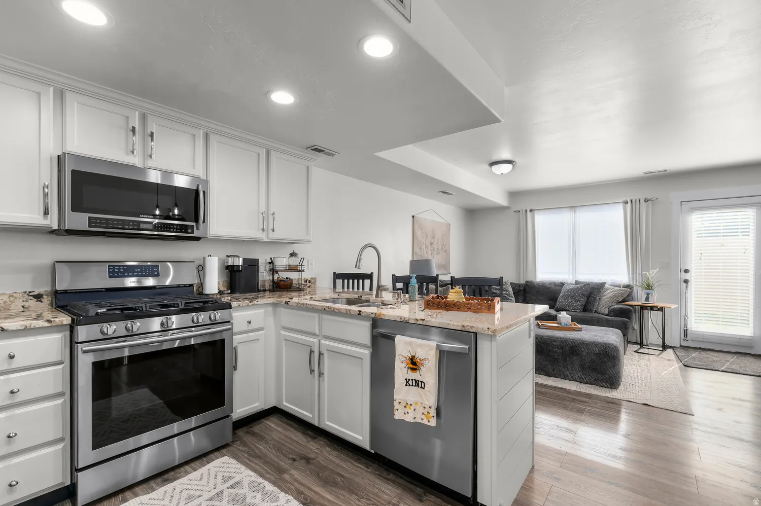 Open-concept kitchen featuring white cabinetry, stainless steel appliances, and a central island with a sink