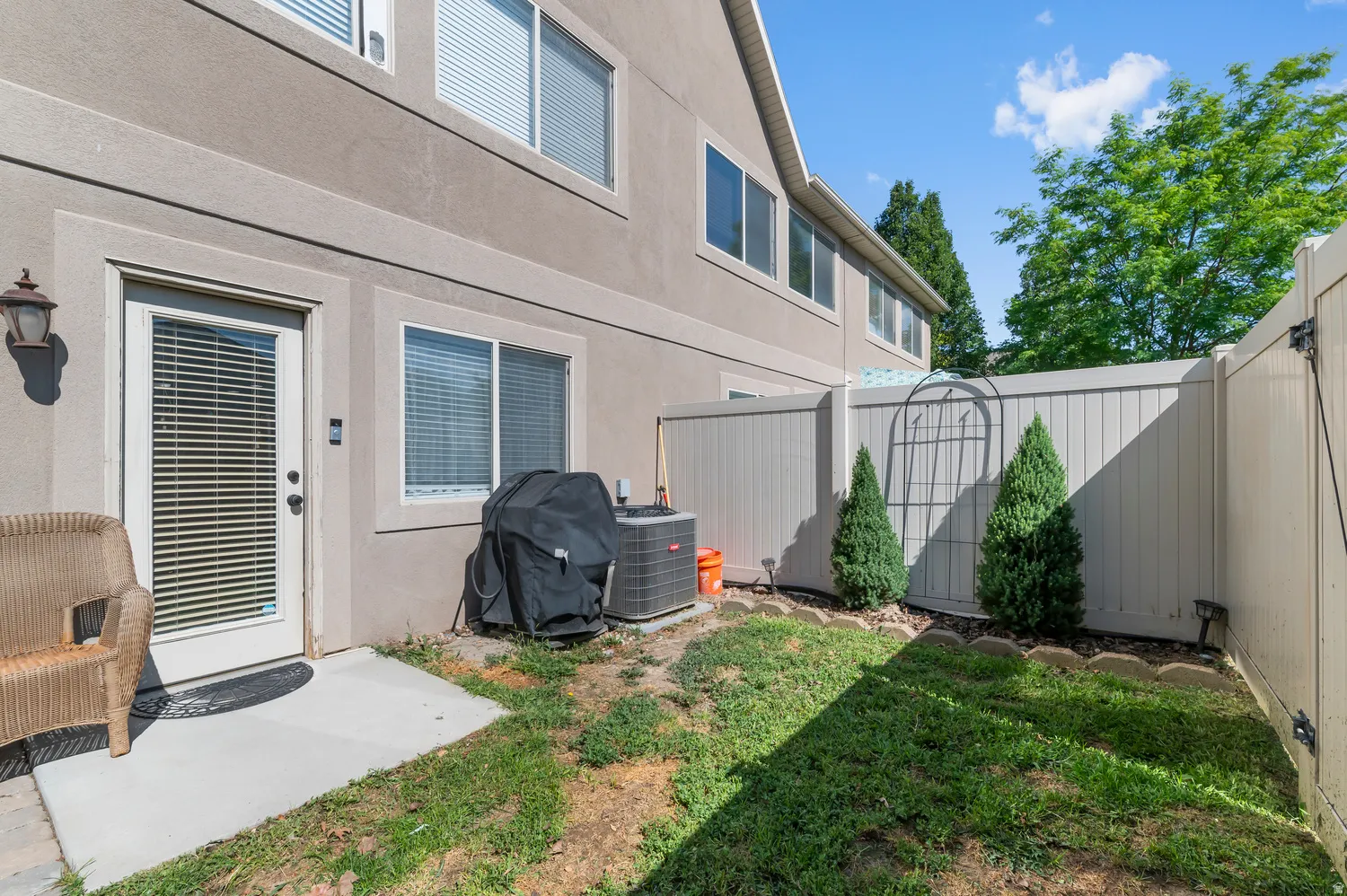 Private outdoor space featuring a concrete patio, green lawn, full-height privacy fencing, and exterior wall-mounted lighting