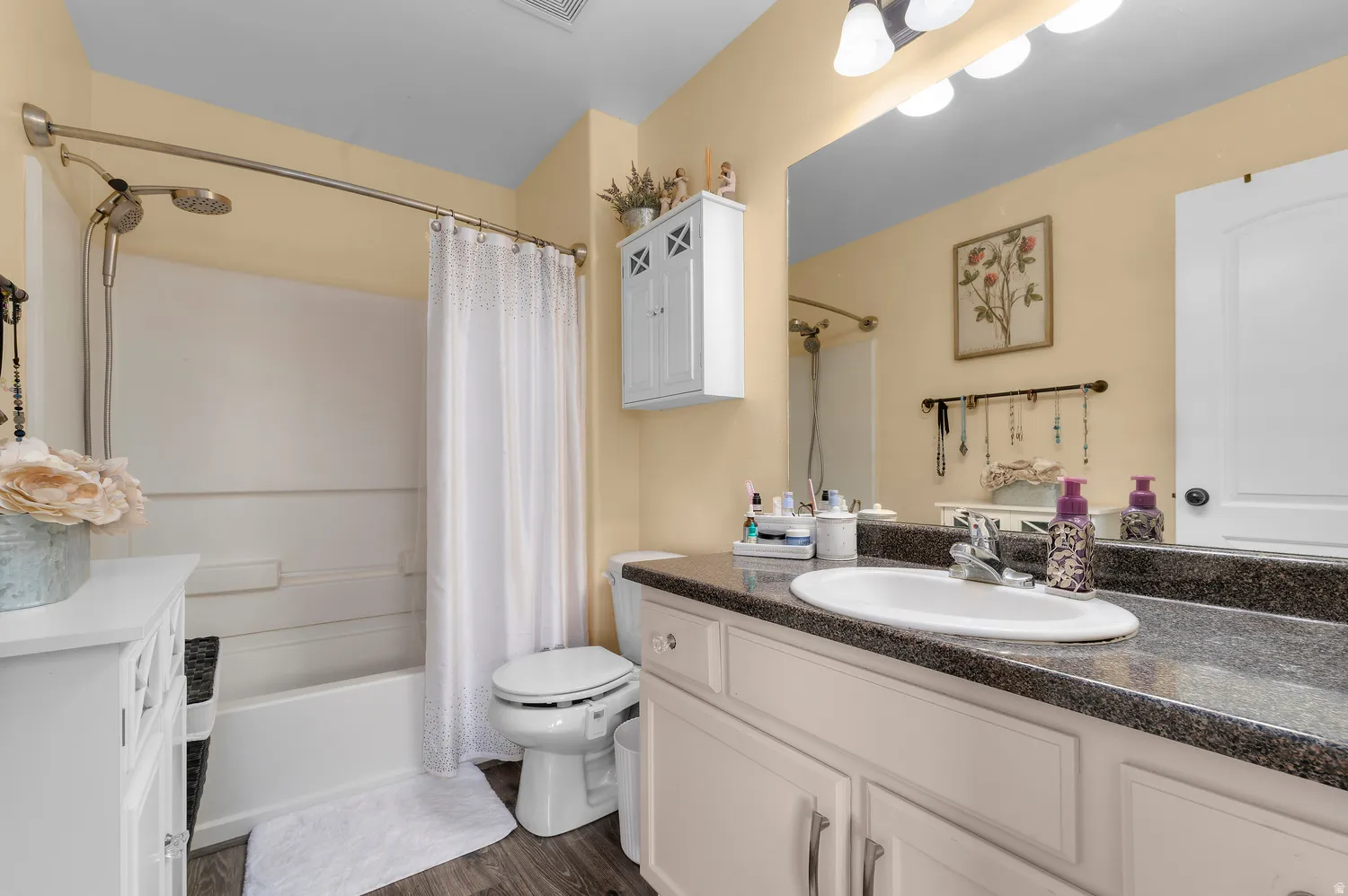 Full bathroom featuring a tub/shower combination with a brushed nickel showerhead, a single vanity with a dark speckled countertop and undermount sink, and wood-finish flooring