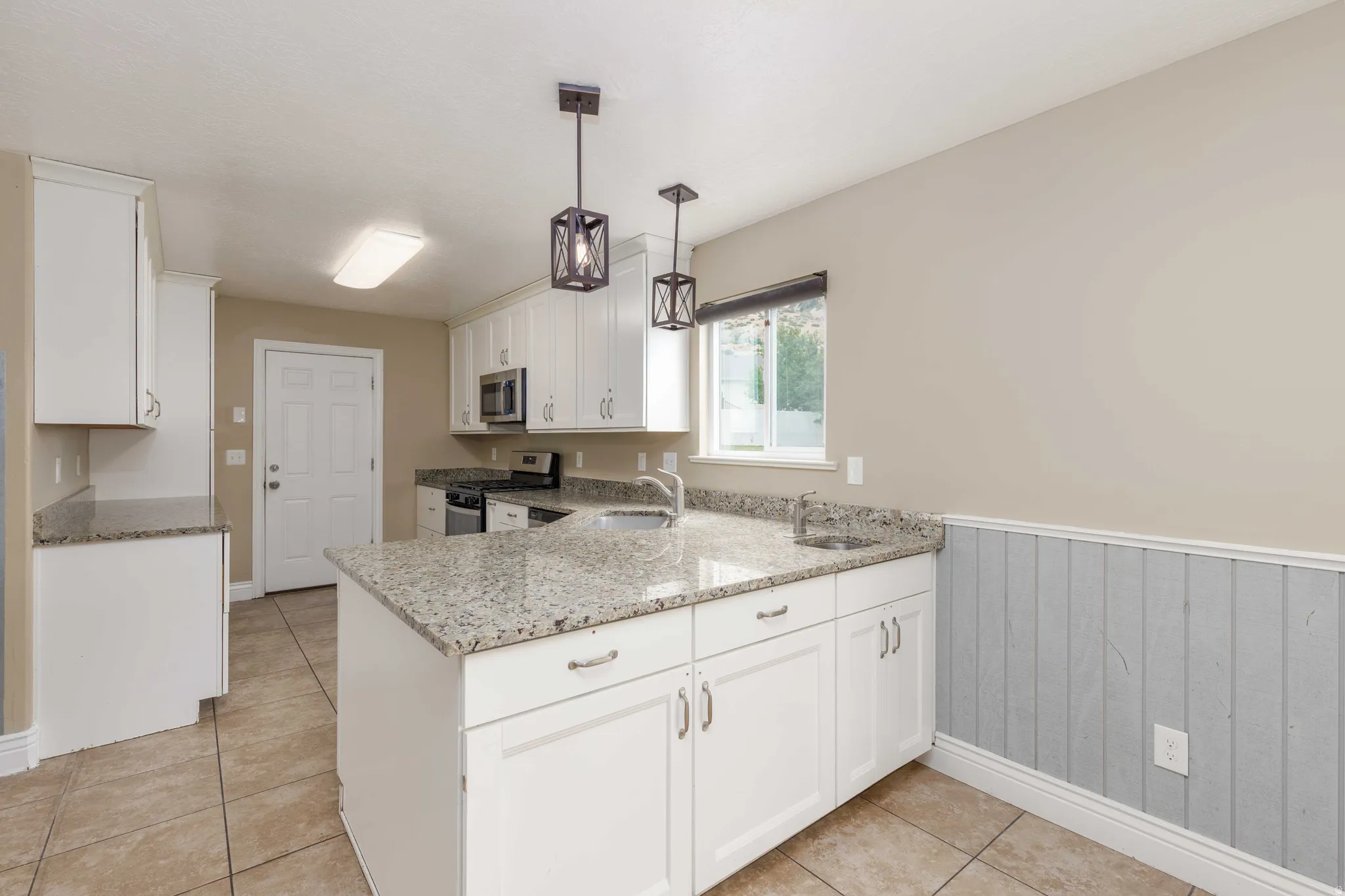 Kitchen featuring white cabinetry, granite countertops, stainless steel appliances, tiled flooring, and industrial-style pendant lighting