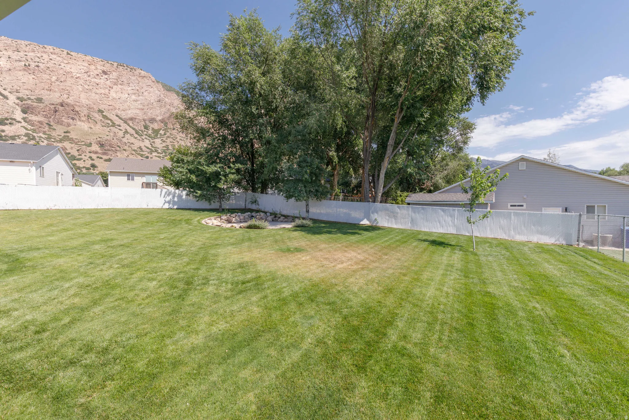 Expansive lawn area featuring a white privacy fence, mature trees, a small rock garden, and a distant mountain backdrop