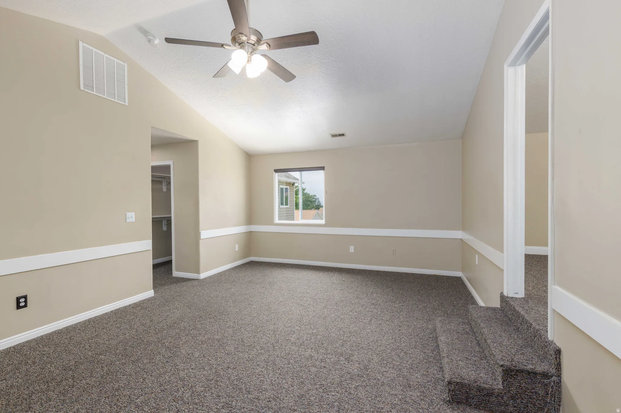 Carpeted room featuring a vaulted ceiling and a ceiling fan with integrated lighting