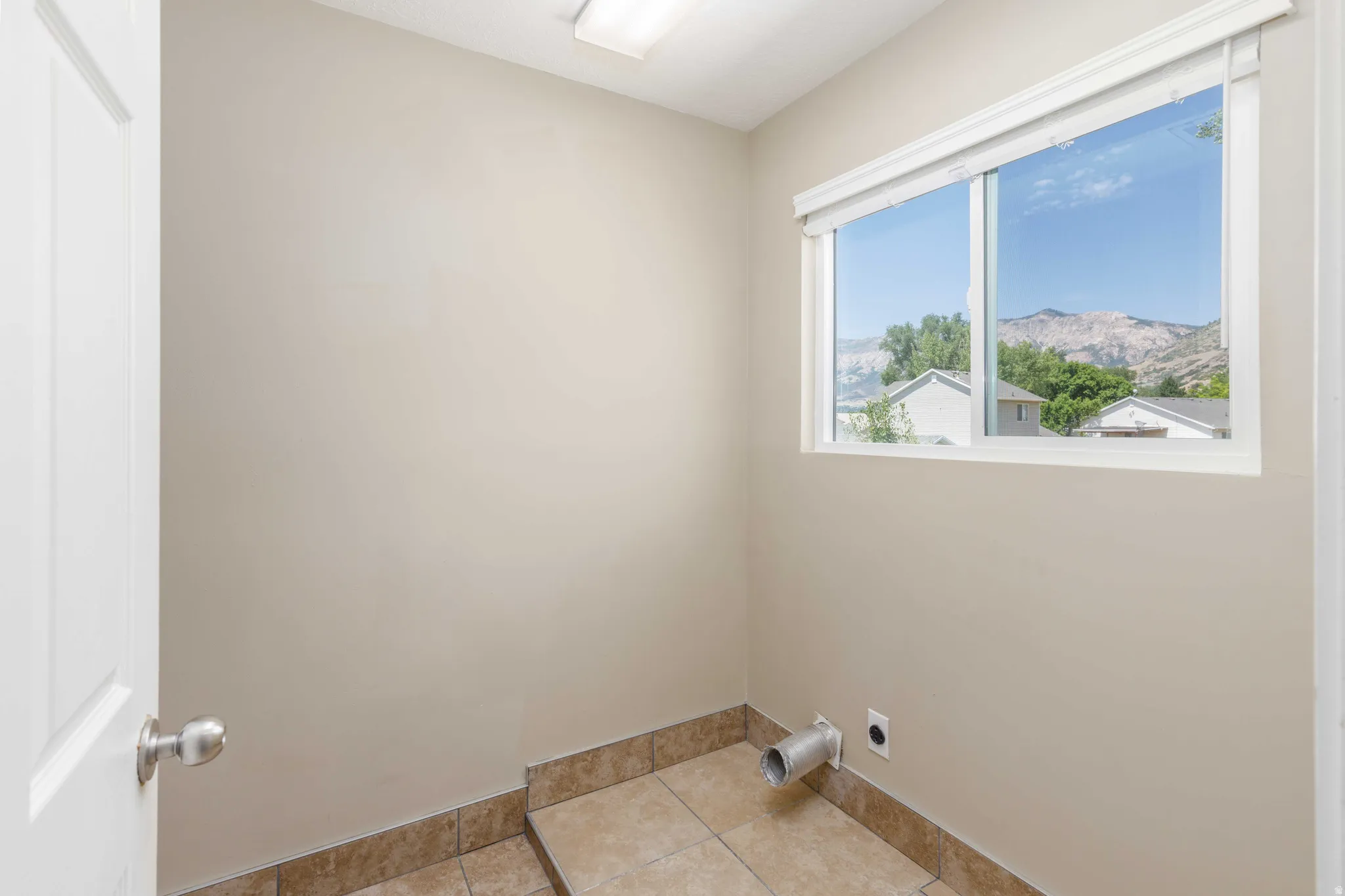 Utility room featuring neutral wall tones, tiled flooring, a large window, and visible utility connections