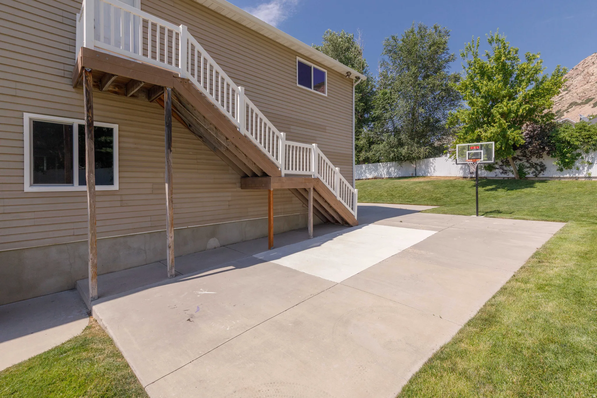 Rear exterior featuring a large concrete patio, a basketball hoop, and a terraced lawn