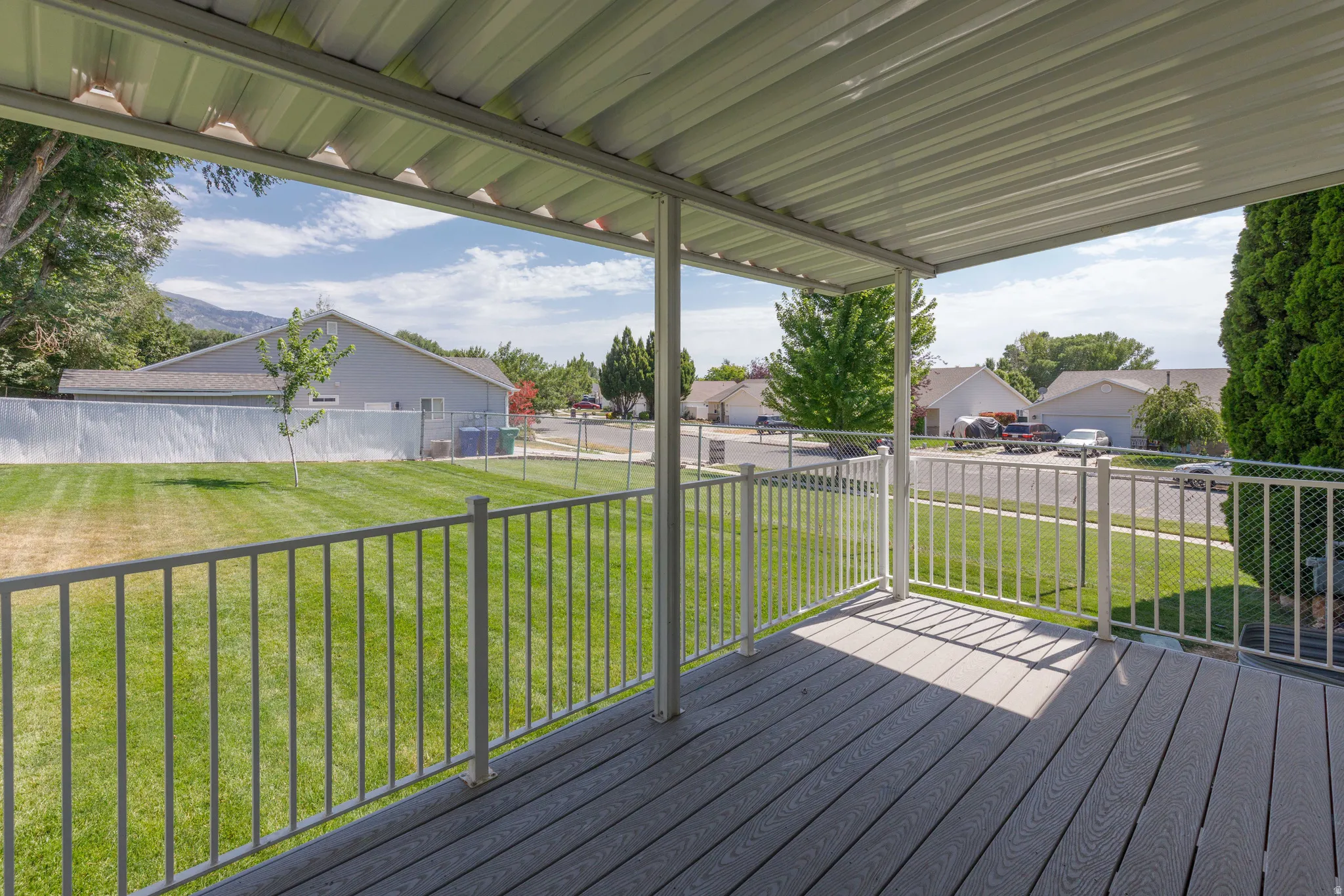 Covered deck featuring composite decking and metal railings, overlooking a fenced backyard and residential street