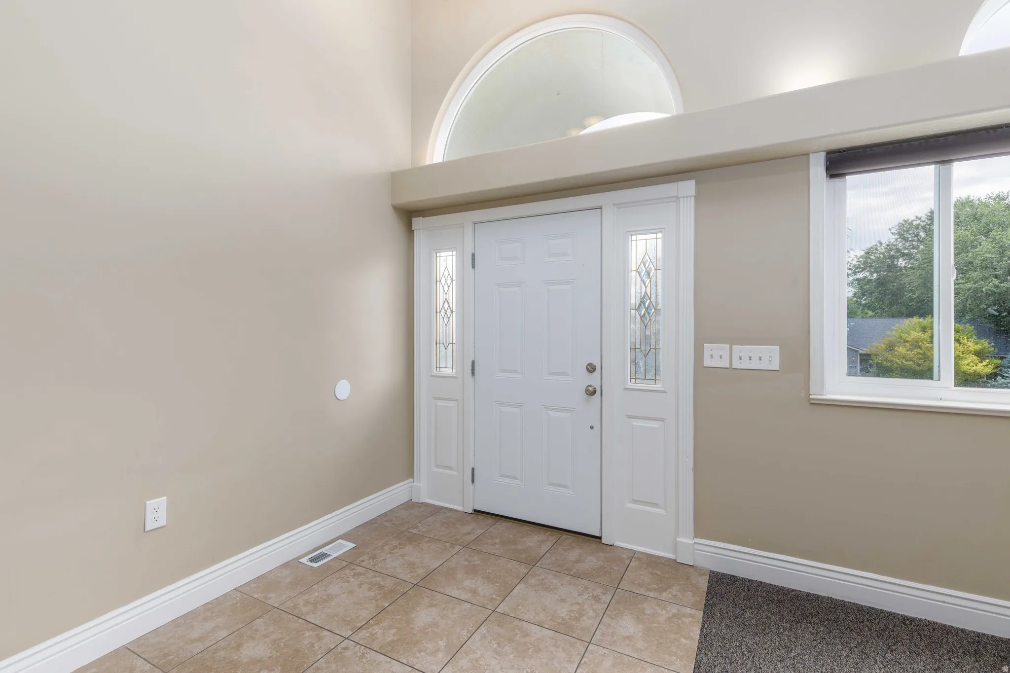 Entryway featuring a white paneled door with decorative sidelights, a large arched transom window, and a rectangular window with exterior views