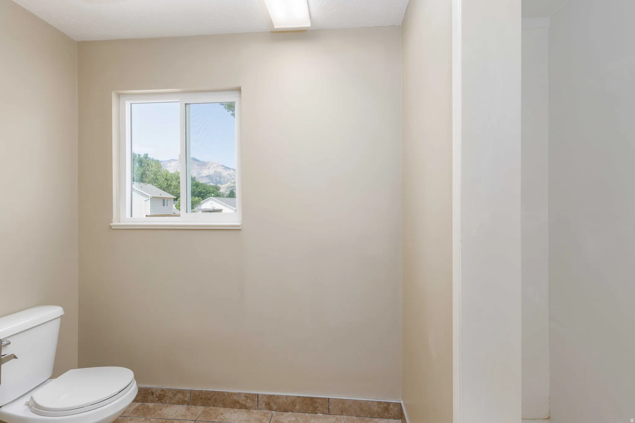 Bathroom featuring a white toilet, neutral wall paint, and tiled flooring