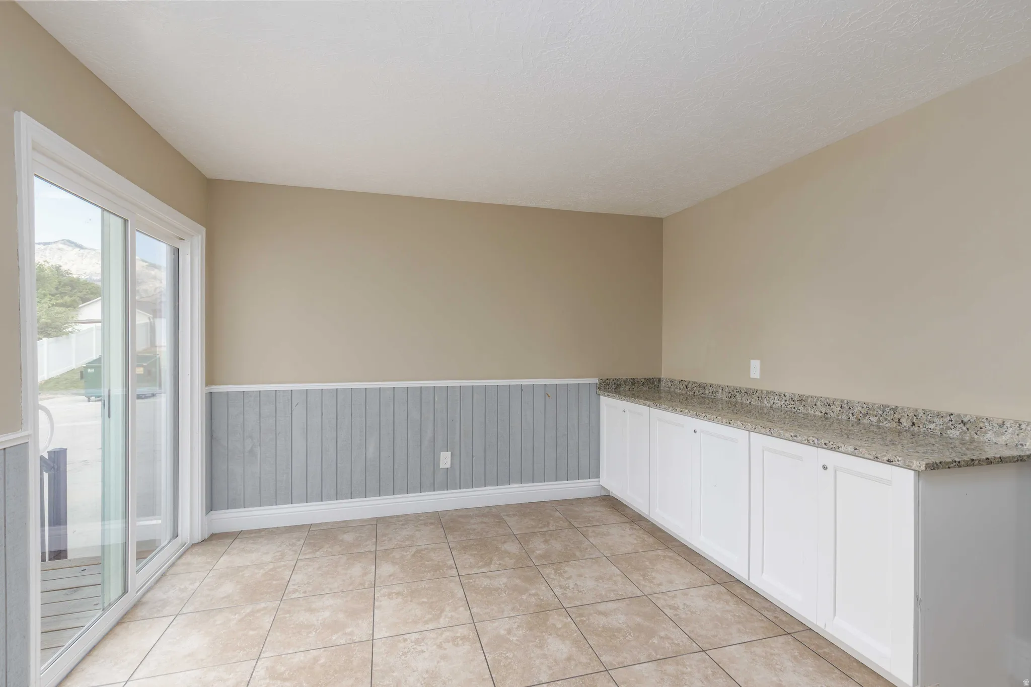 Room featuring ceramic tile flooring, a built-in white cabinet unit with a stone-look countertop, and a sliding glass door