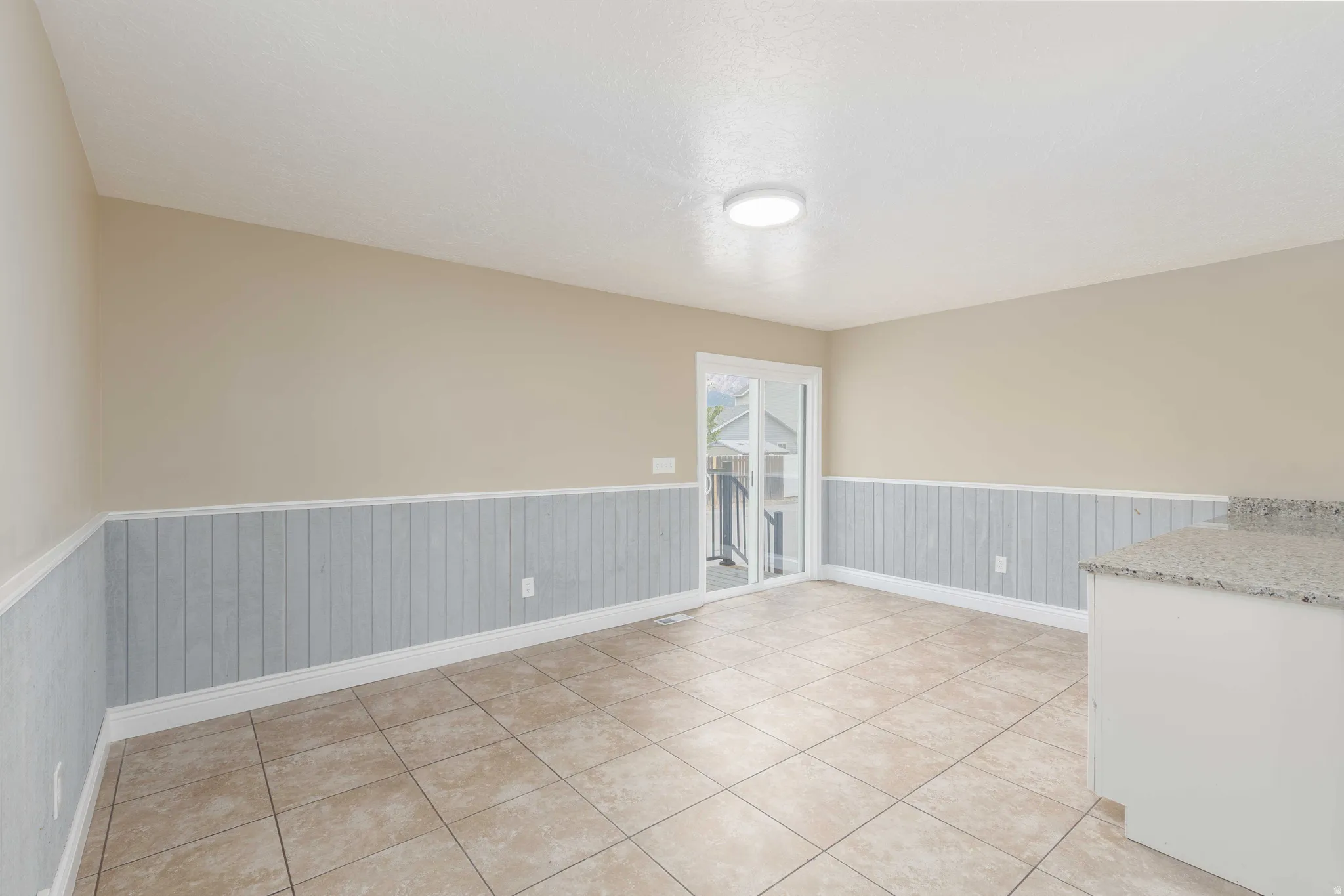 Expansive room featuring neutral-toned walls, wainscoting detail, durable tile flooring, and a sliding glass door for outdoor access
