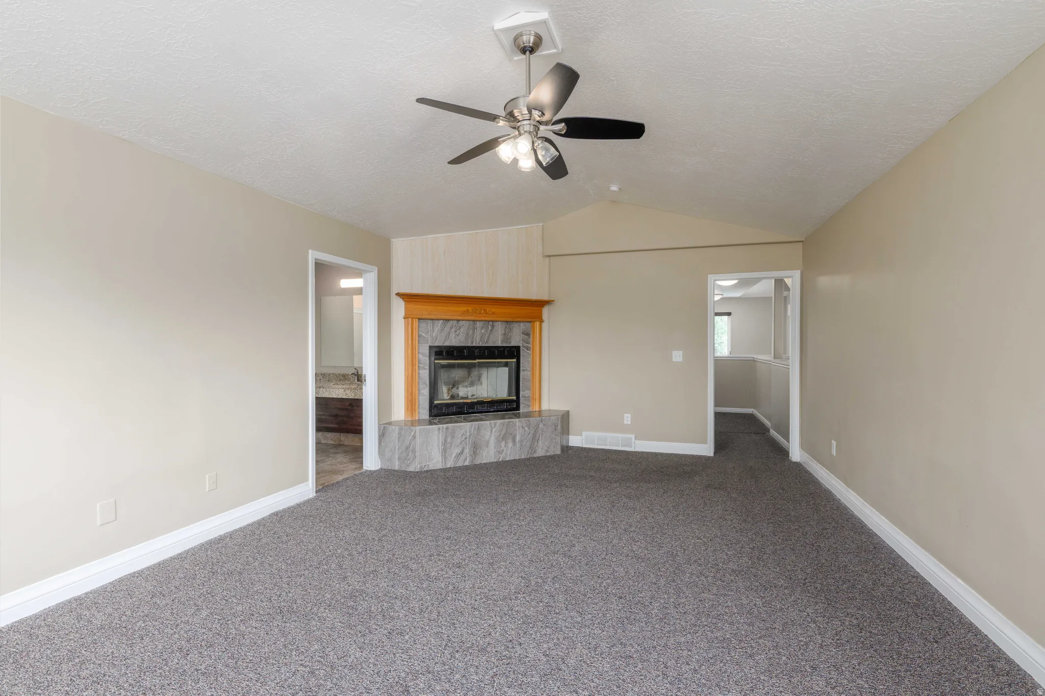 Living area with vaulted ceiling, ceiling fan, and corner fireplace featuring a wood mantel and tile surround