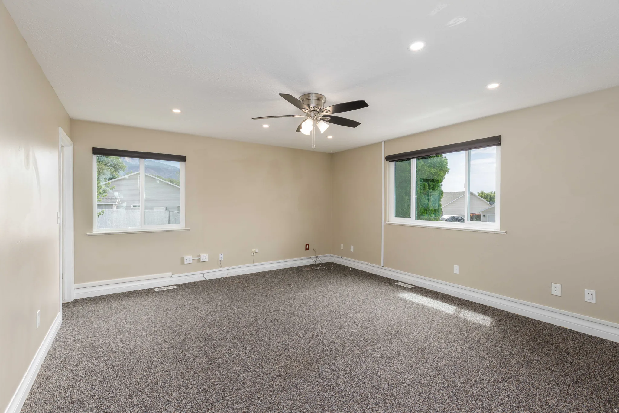 Spacious room featuring neutral paint, gray carpet, two windows, recessed lighting, and a ceiling fan with integrated lighting