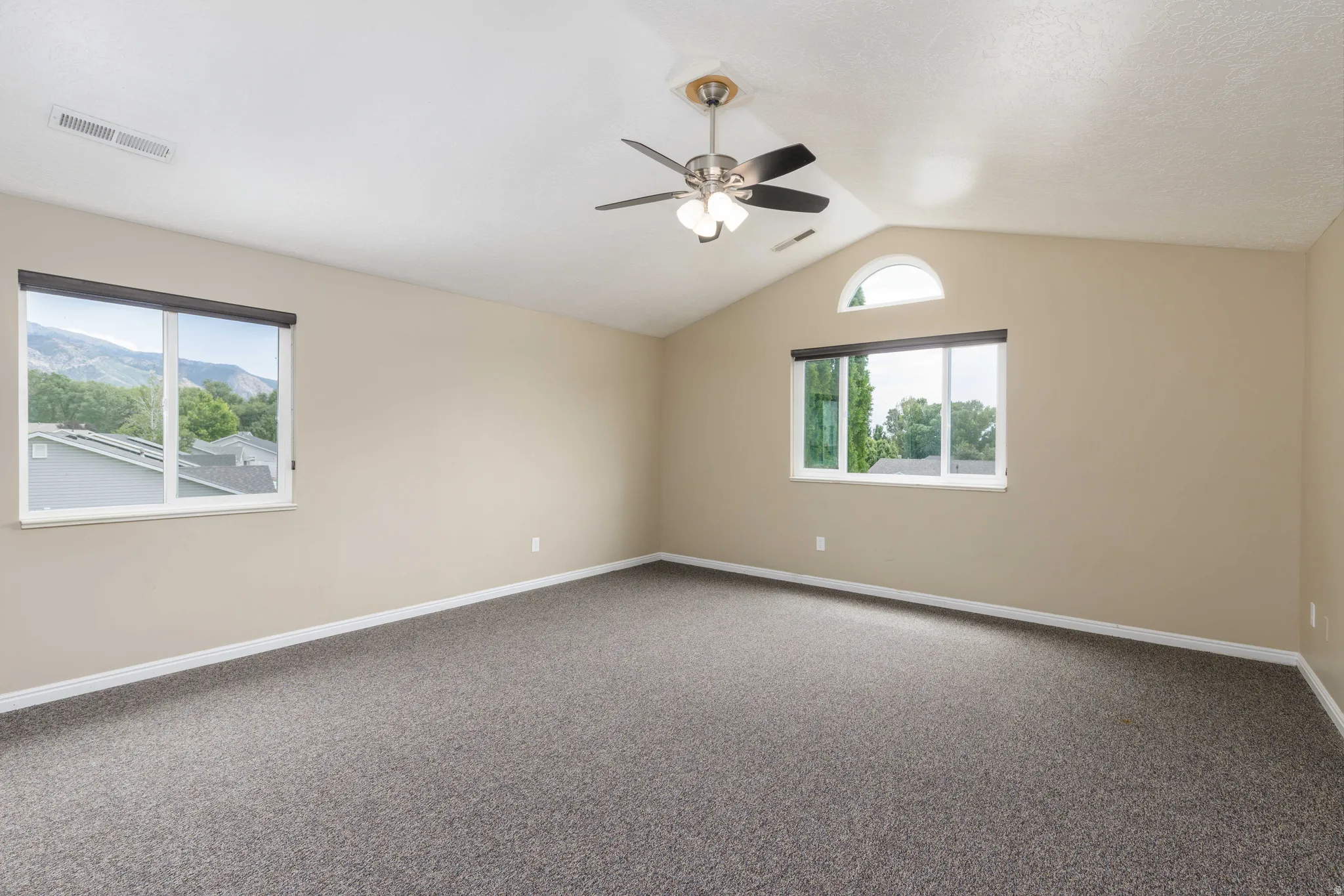 Spacious room with vaulted ceilings, neutral-toned walls, and dark gray carpeting