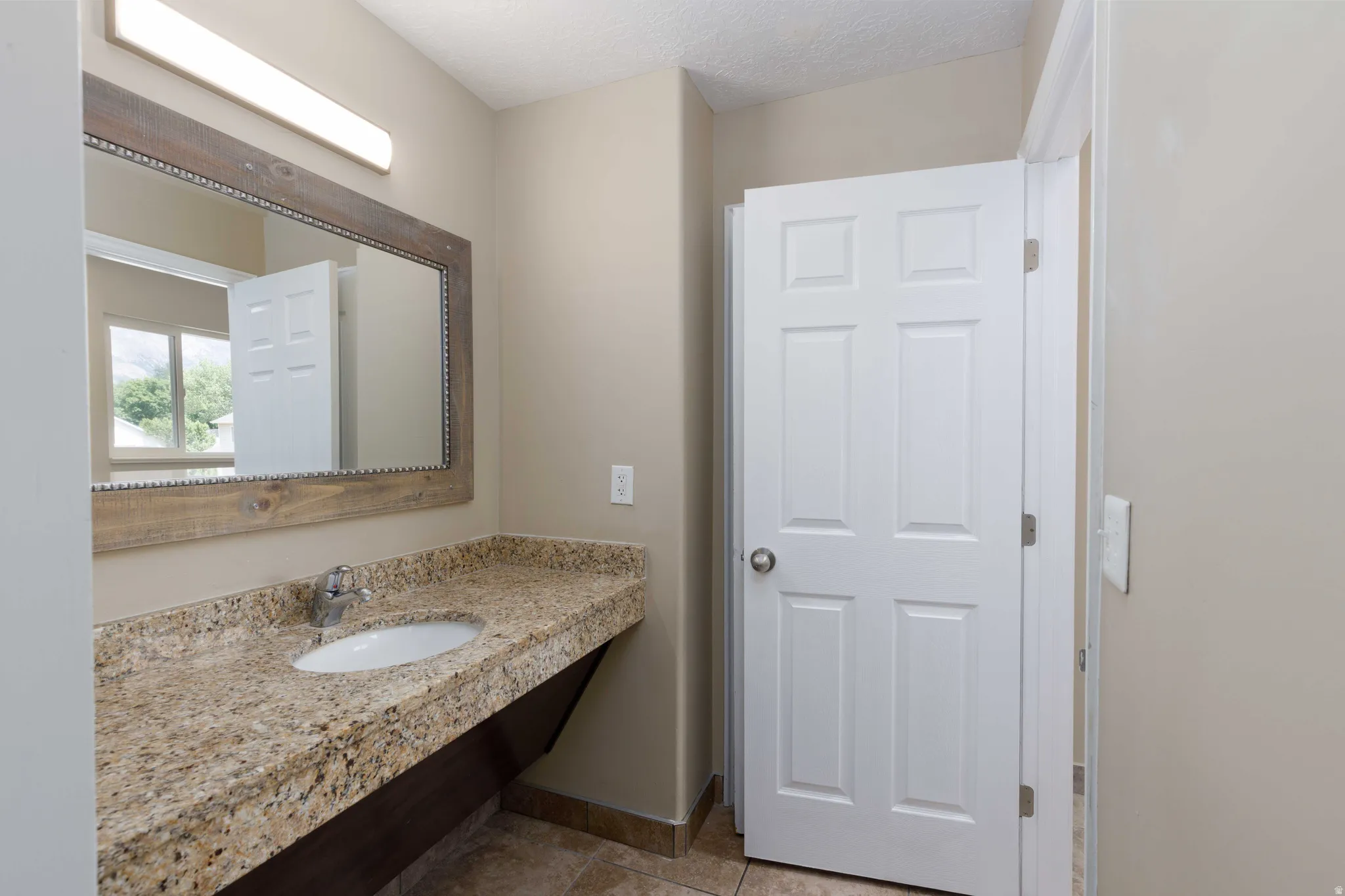 Bathroom vanity featuring a speckled countertop, undermount sink, and a framed mirror with an overhead light fixture