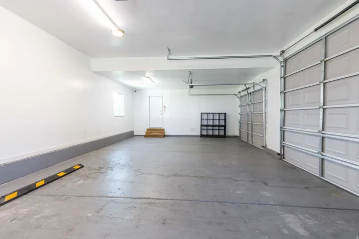 Spacious garage featuring a concrete floor, two overhead doors, interior access door with wooden steps, and a side window