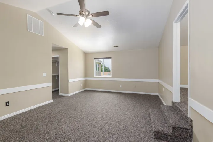 Carpeted room featuring a vaulted ceiling and a ceiling fan with integrated lighting