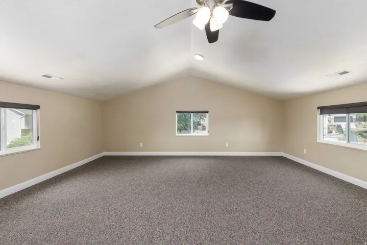 Spacious room featuring vaulted ceilings, neutral-toned walls, and dark textured carpeting